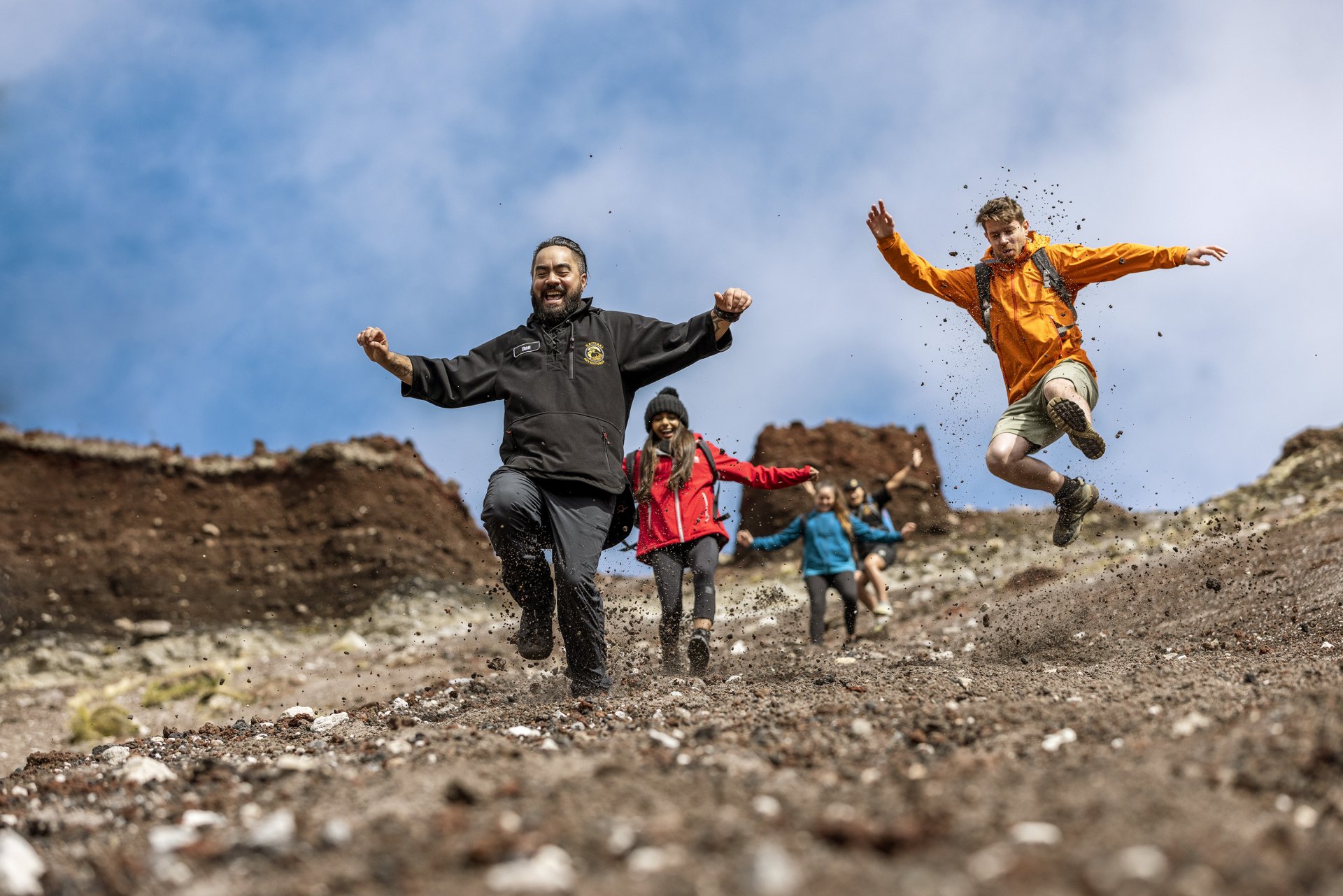 220302-kaitiaki-adventures_mount-tarawera-guided-walk-jumping-down-scree-front-on_credit-miles-holden